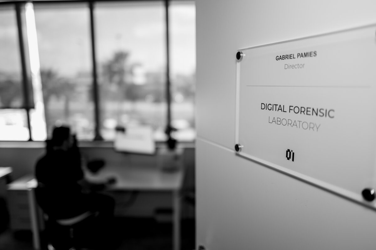 Placa del laboratorio de informática forense de 0Invader en Elche, con un analista trabajando al fondo